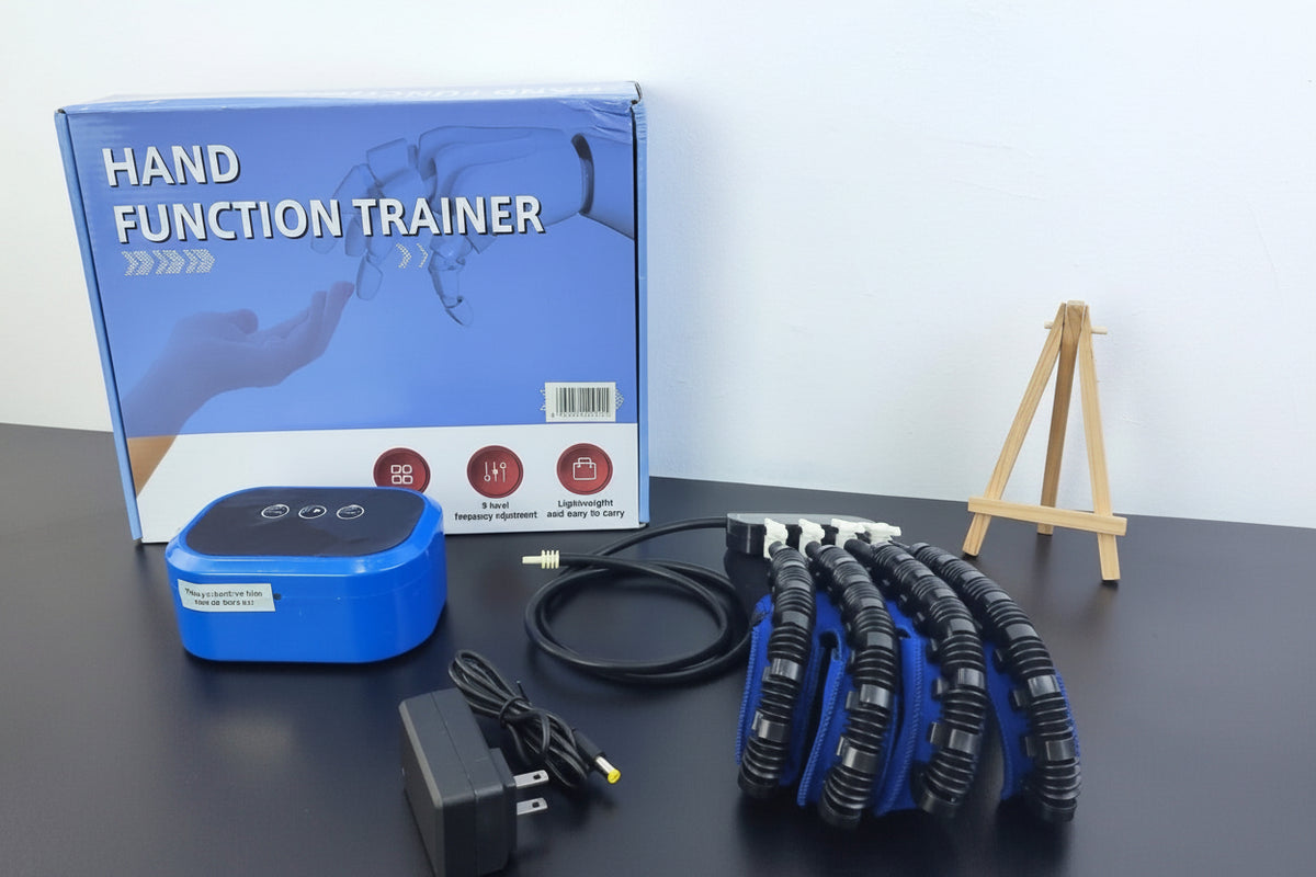 Hand function trainer set displayed on a dark tabletop with its retail box, blue electronic controller, black power adapter, coiled cable, and a black-and-blue robotic hand. A small sign reading 'WE ARE H&R' is visible, and the H&R-MEDICINE logo appears in the top left.