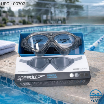 Speedo swim goggles resting on top of their retail box, placed on the edge of an outdoor swimming pool with pool lanes and water visible in the background.
