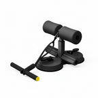 A black foam exercise device with suction cup base and a T-bar handle with a yellow accent, shown on a light wood floor in a bright room.