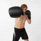 A shirtless man wearing black boxing gloves and black athletic shorts poses against a light gray studio background. The brand logo 'HER SPORT' appears in the top-left corner,