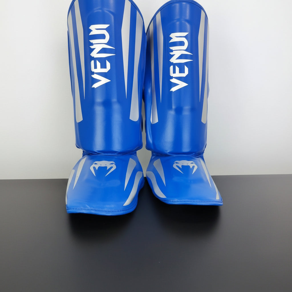 Blue Venum shin guards with white branding, displayed on a dark surface 
