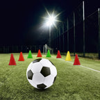 Soccer ball on a grass field with colorful cones under stadium lights