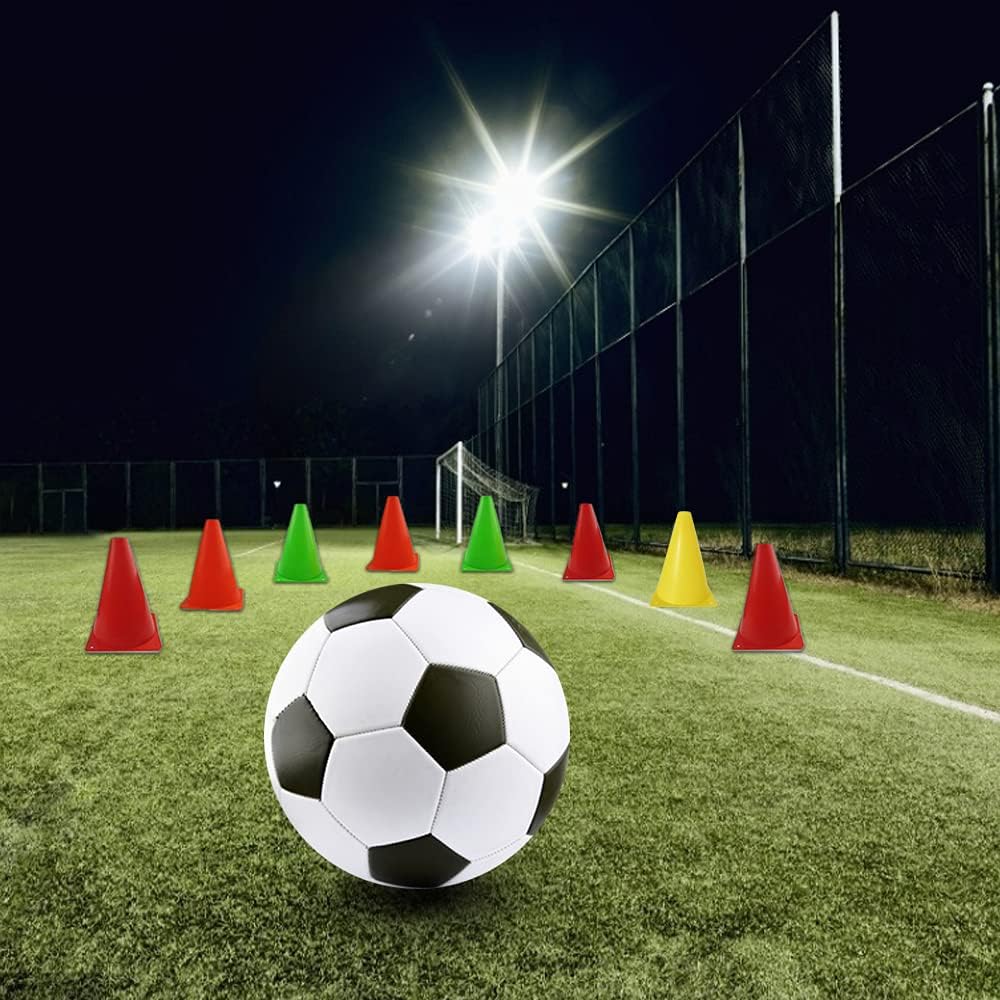 Soccer ball on a grass field with colorful cones under stadium lights