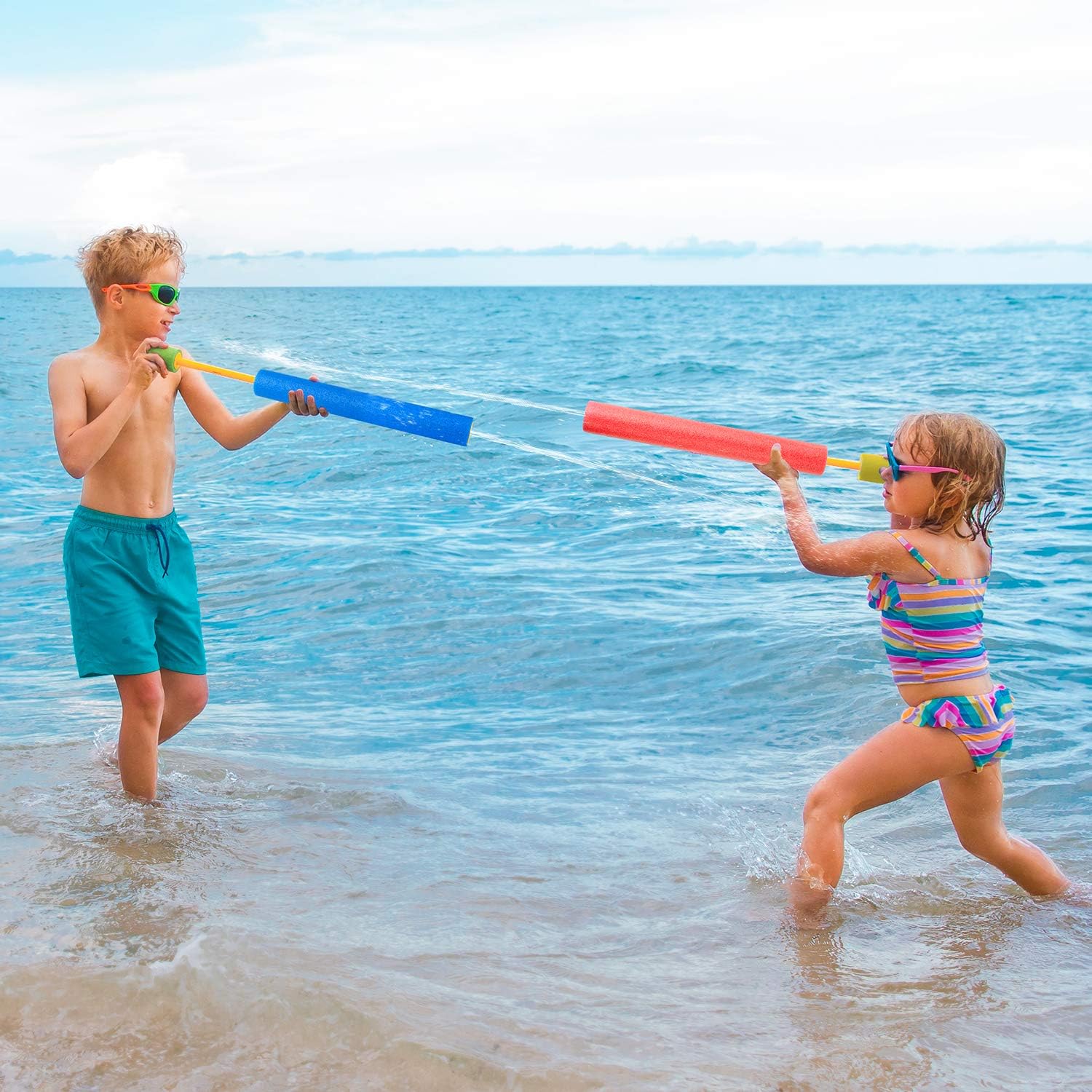 guns in shallow ocean water. A boy on the left wears teal swim trunks and green-tinted sunglasses, holding a blue water gun.